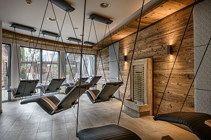 Ein Raum mit hängenden Liegestühlen, Holzwänden und sanfter Beleuchtung, der eine entspannende, moderne Atmosphäre bietet.